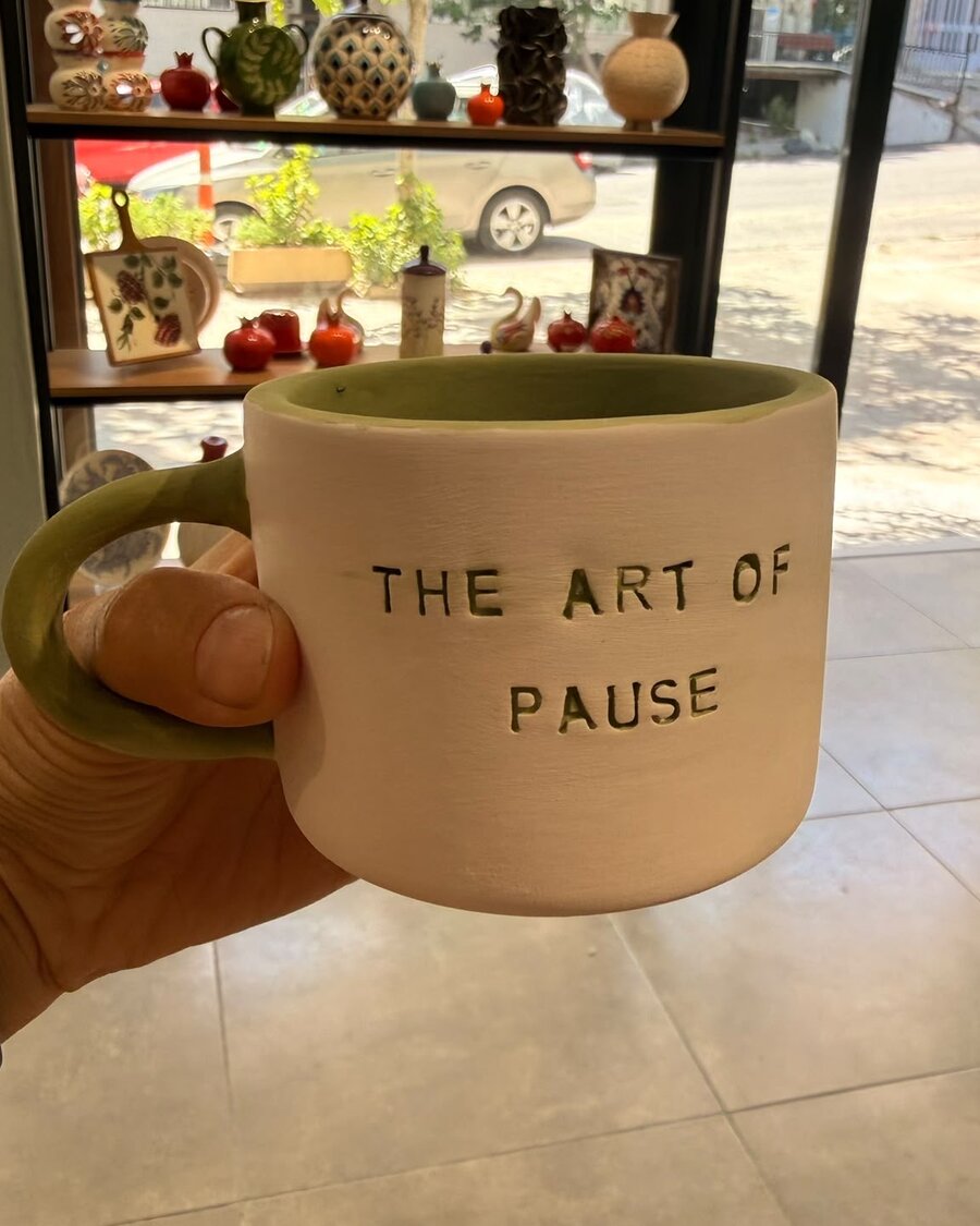 “The Art of Pause” kupası — fırından çıkmış, adaçayı sırlı hâliyle atölye vitrininin önünde